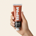 Hand holding a metal tube of BPM deodorant against a beige background